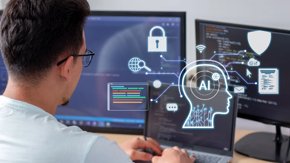 Digitaliseringen må spille på lag med de ansattes tause kunnskap. Mann arbeider på to dataskjermer med visuelle representasjoner av AI og datasikkerhetsteknologier.
