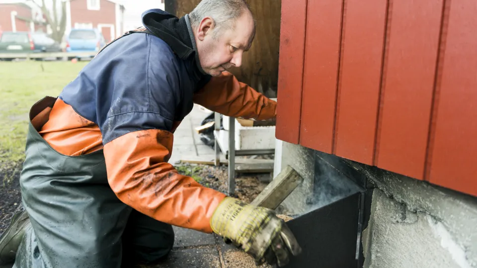 Alle som kan, skal arbeide En mann iført arbeidstøy jobber med fundamentet på en rød bygning. Han bruker verktøy og ser konsentrert ut.