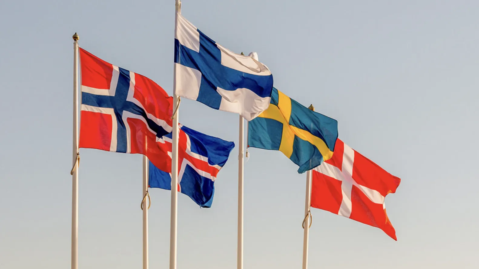 Nye tal om indvandrere og integration i Norden Fem flag, der repræsenterer de nordiske lande, svajer i vinden på en lys himmelbaggrund. De viser flagene fra Norge, Finland, Island, Sverige og Danmark, som symboliserer nordisk fællesskab.