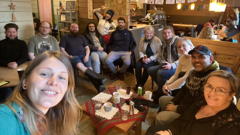 Third space event at a coffee house in Ísafjörður, autumn 2024 A group of people gathered around a table in a cozy café, smiling for a group photo. The café has warm wooden decor and festive holiday accents.