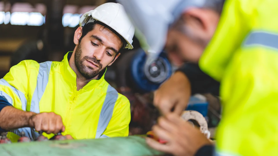 Flexibel validering av generella kompetenser Arbetare i skyddskläder och hjälm arbetar med industriellt maskineri i en fabriksmiljö.