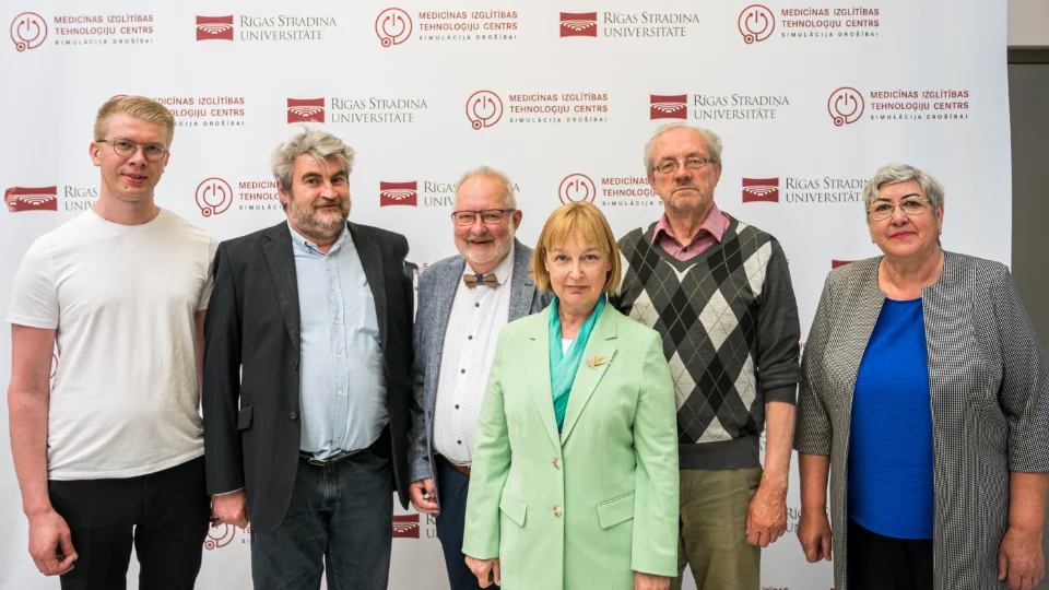 Nordplus projekt – age is not an obstacle III A group of six people posing in front of a backdrop with "Rīga Stradiņš University" and "Medical Education Technology Center" logos. They are dressed in a mix of casual and formal attire, smiling at the camera.