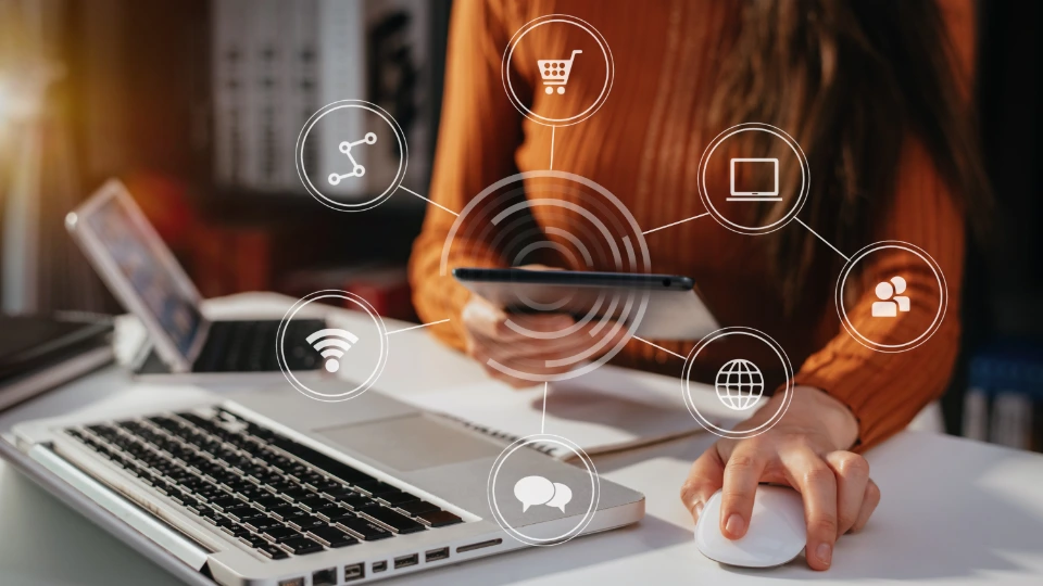 Kvinna som använder surfplatta vid skrivbord med bärbar dator och digitala ikoner för nätverk, e-handel och kommunikation.