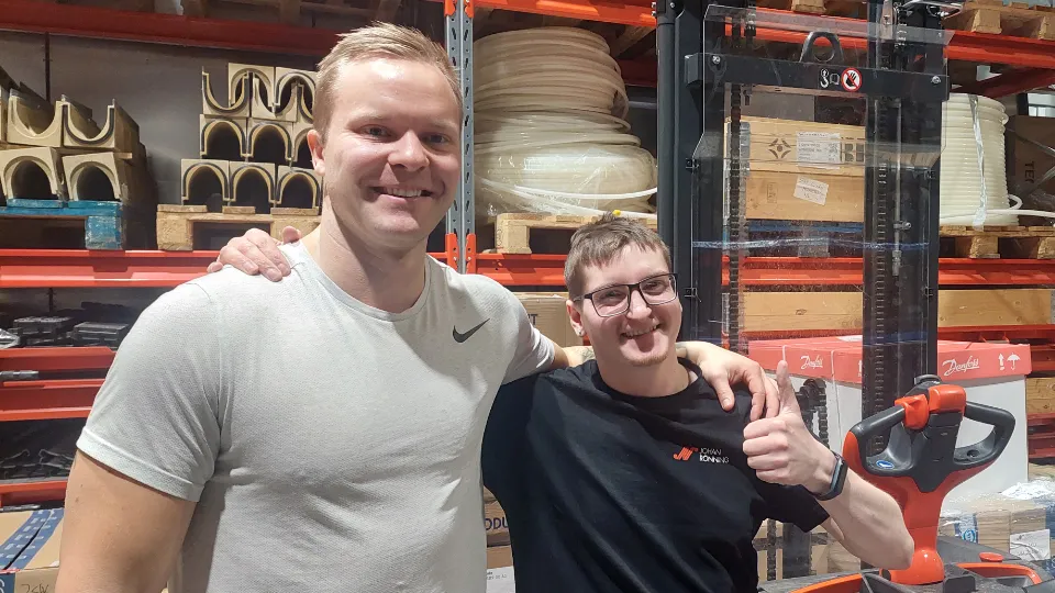 Fannar Freyr Gíslason og Daníel Smári Bjarnason smiler og poserer sammen på et lager med hyller, paller og industrimateriell i bakgrunnen.
