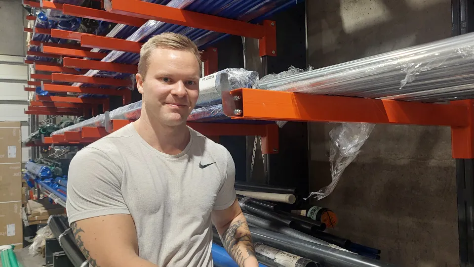 Fannar Freyr Gíslason i lysegrå t-skjorte ved reoler med lange metallrør i et industrilager.