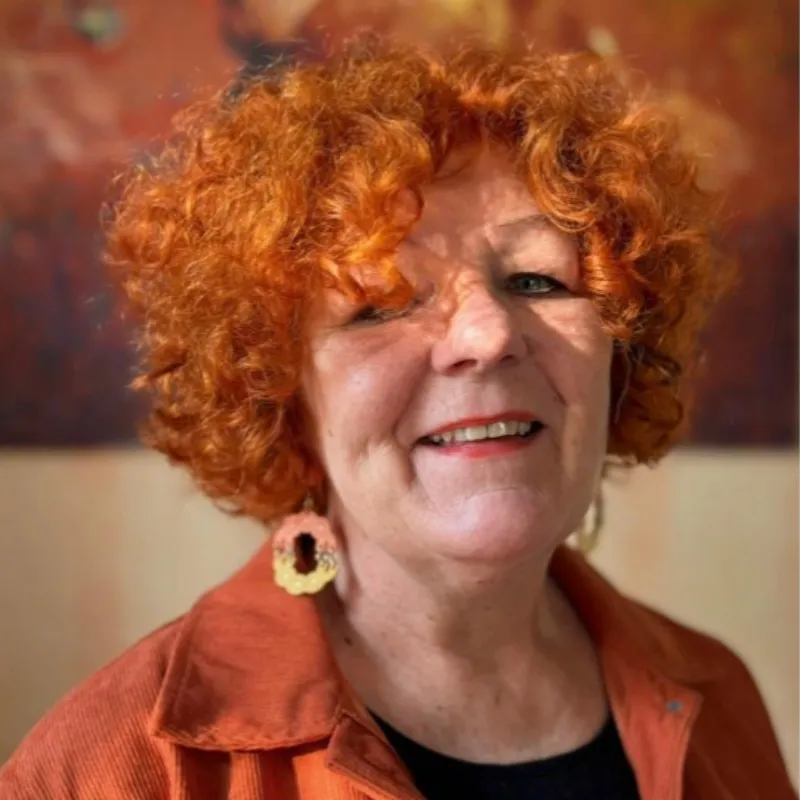Maria Ingman med lockigt rött hår, iförd orange jacka och handgjorda örhängen.