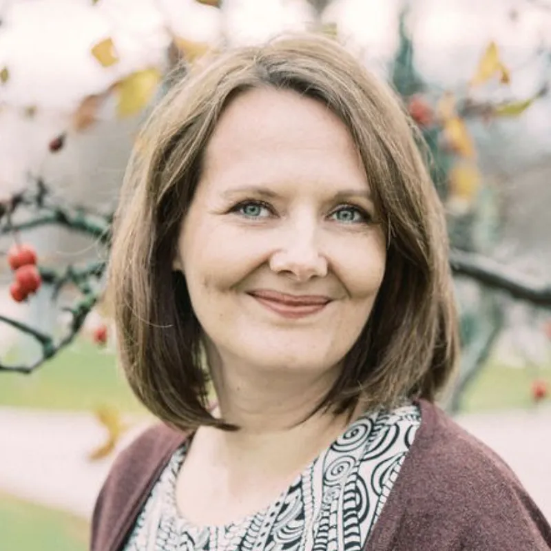 Sanna Saarimaa med axellångt brunt hår, stående utomhus framför ett träd med röda bär.