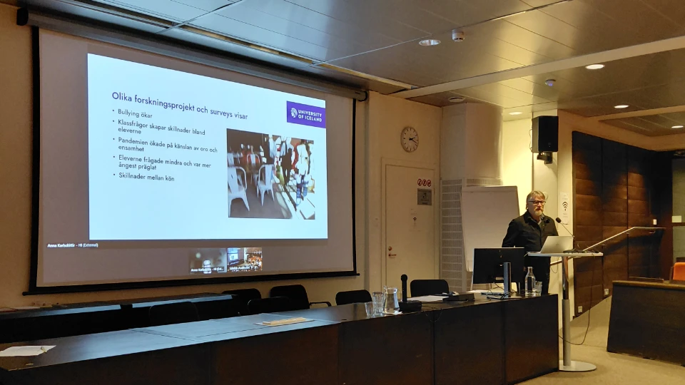 Bo Nygård talar vid ett podium under lansering av NLL:s samarbetsprojekt på Åland, med presentation projicerad på stor skärm i konferenslokal.
