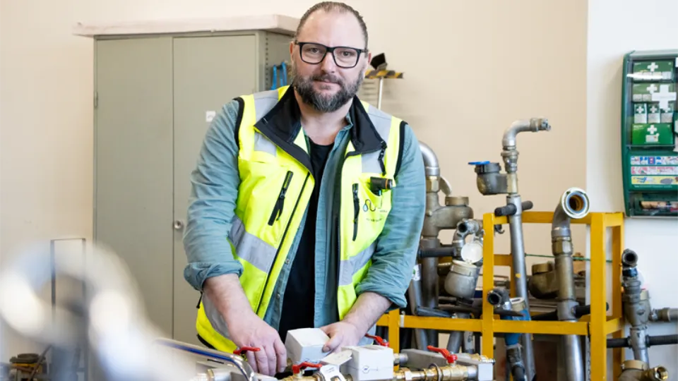 Medelålders man med trimmat skägg och glasögon i en verkstad.