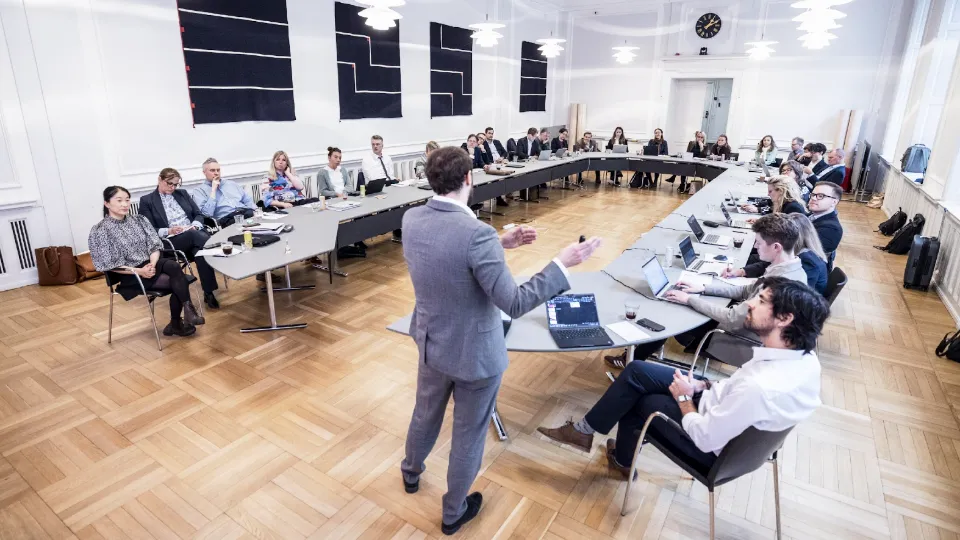Representatives from social partners, government agencies and research institutions met in Copenhagen Business meeting in a bright conference room with a speaker presenting to seated attendees around U-shaped tables.
