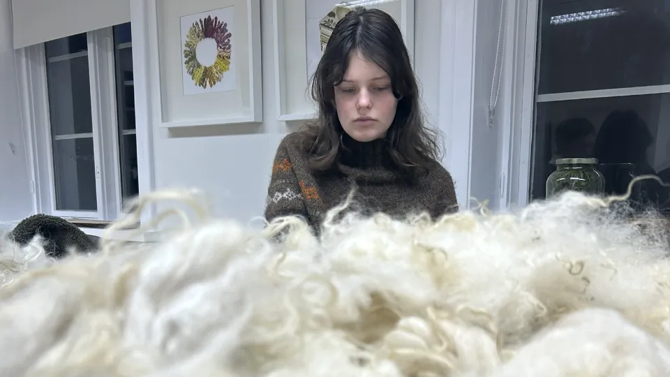 Þorgerður Þorkelsdóttir sitter innendørs og arbeider med lys ull på et bord.