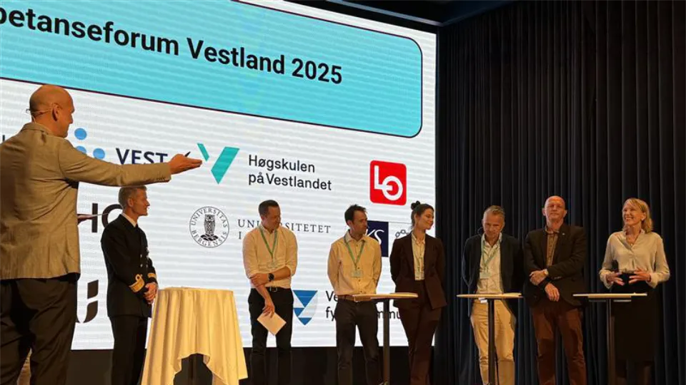 Paneldebatt på scene under Kompetanseforum Vestland 2025 med flere deltakere og presentasjonsskjerm i bakgrunnen.