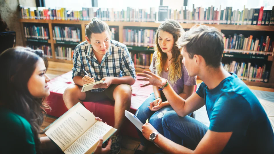 DFS i nyt partnerskab om lokalt beredskab i Danmark Fire unge sidder i en rundkreds på et bibliotek og diskuterer, mens én læser i en bog og en anden tager noter.
