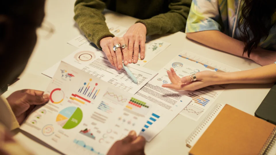 People reviewing reports with graphs and charts on a table during a meeting.