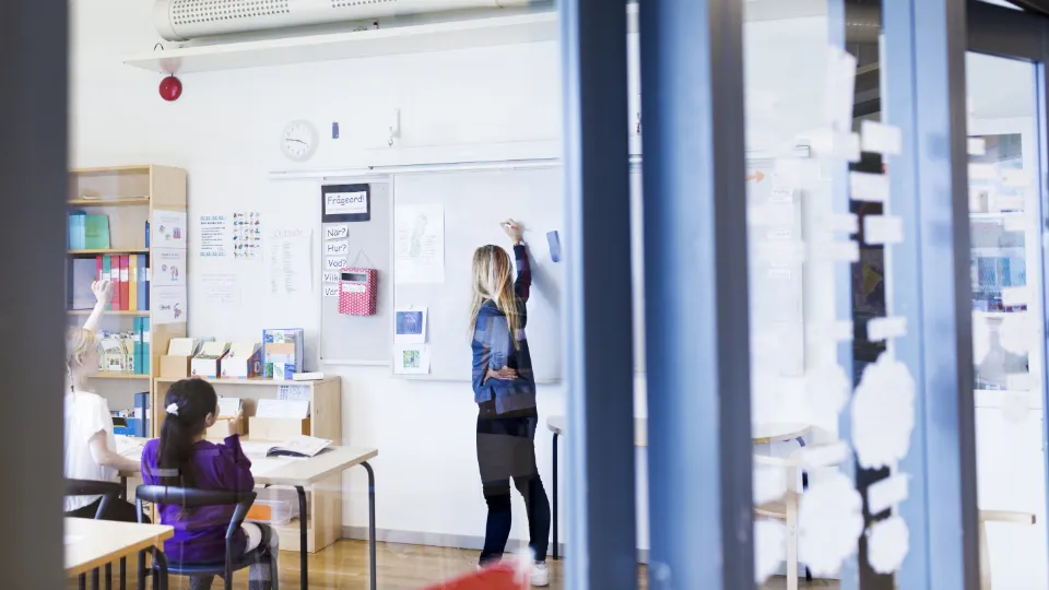 Regeringen godkänner fortsatt arbete med tydligare ramverk för skolor på gränsen mellan skolnivåer En lärare skriver på whiteboardtavlan framför elever i ett ljust klassrum.